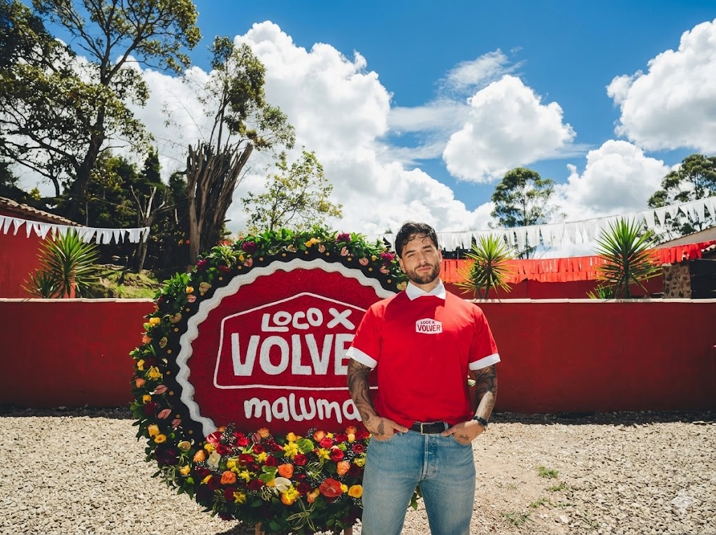Maluma posando junto a una silleta de flores con el logo de su álbum 'Loco x Volver', anunciando que Maluma lanza vallenato este 15 de mayo.